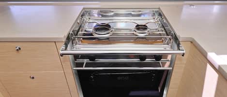 A compact kitchen with a built-in stove and oven, wooden cabinetry, and a window above the stove.