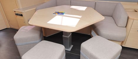 A compact kitchenette with a small table, two cushioned seating areas, and a window above the sink.