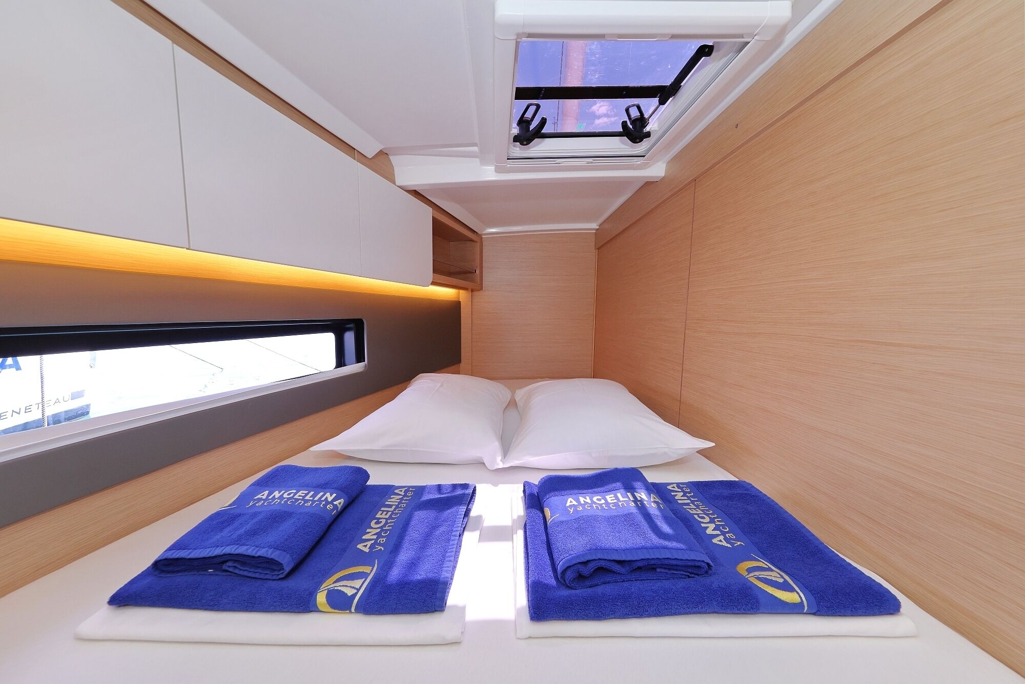 A compact room with a bed, two towels, a window, and a skylight.