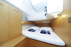 Cabine compacta e bem iluminada com beliche, lambris de madeira e uma mesa pequena com toalhas.