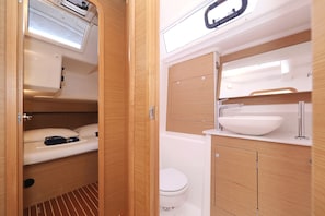 Een kleine badkamer met toilet, wastafel en een klein slaapgedeelte.