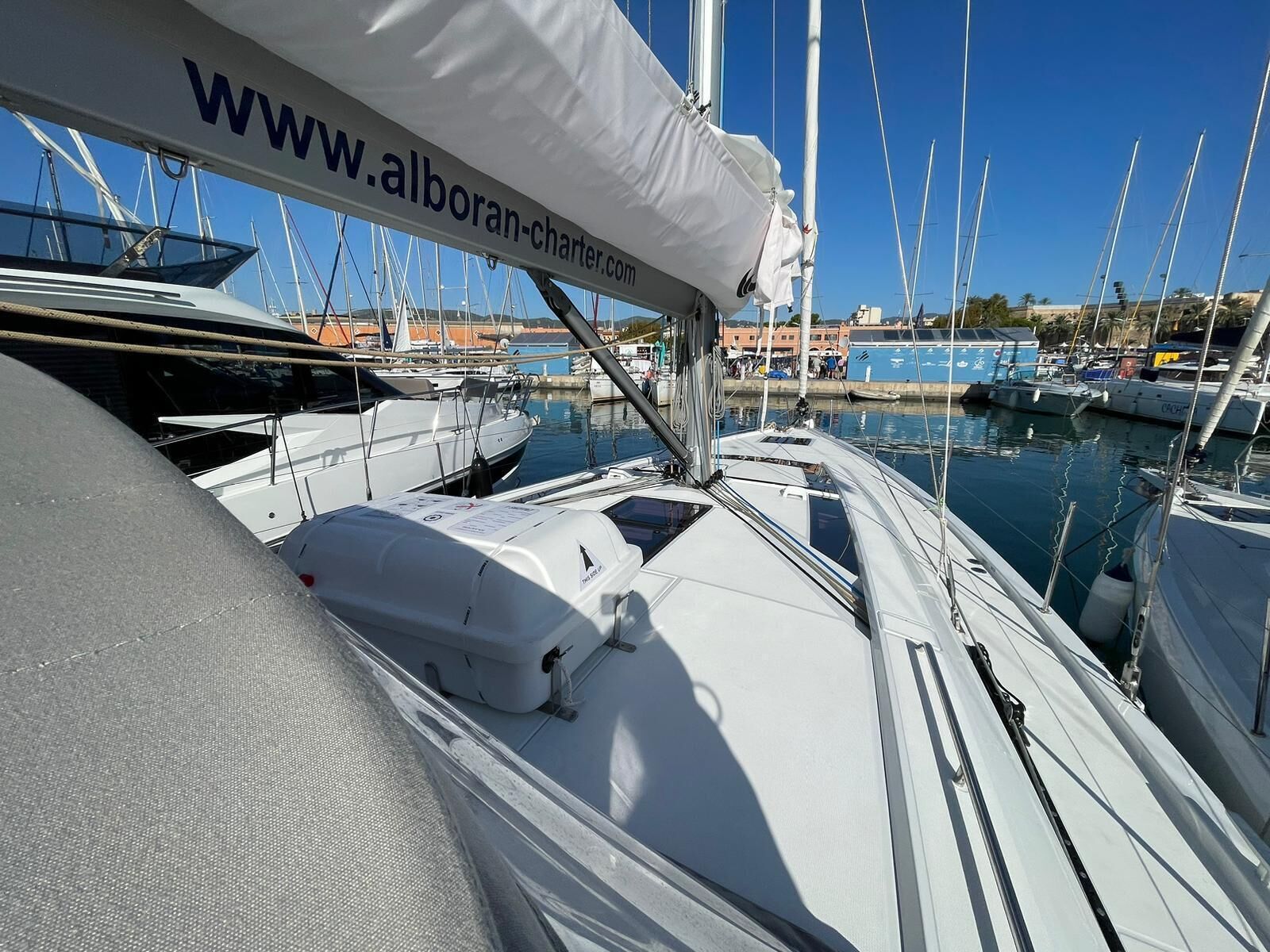 Un port de plaisance où sont amarrés de nombreux voiliers, une bannière de site web et un ciel bleu azur.
