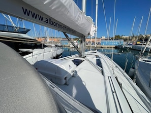 Marina com vários veleiros atracados, um banner de site e céu azul límpido.