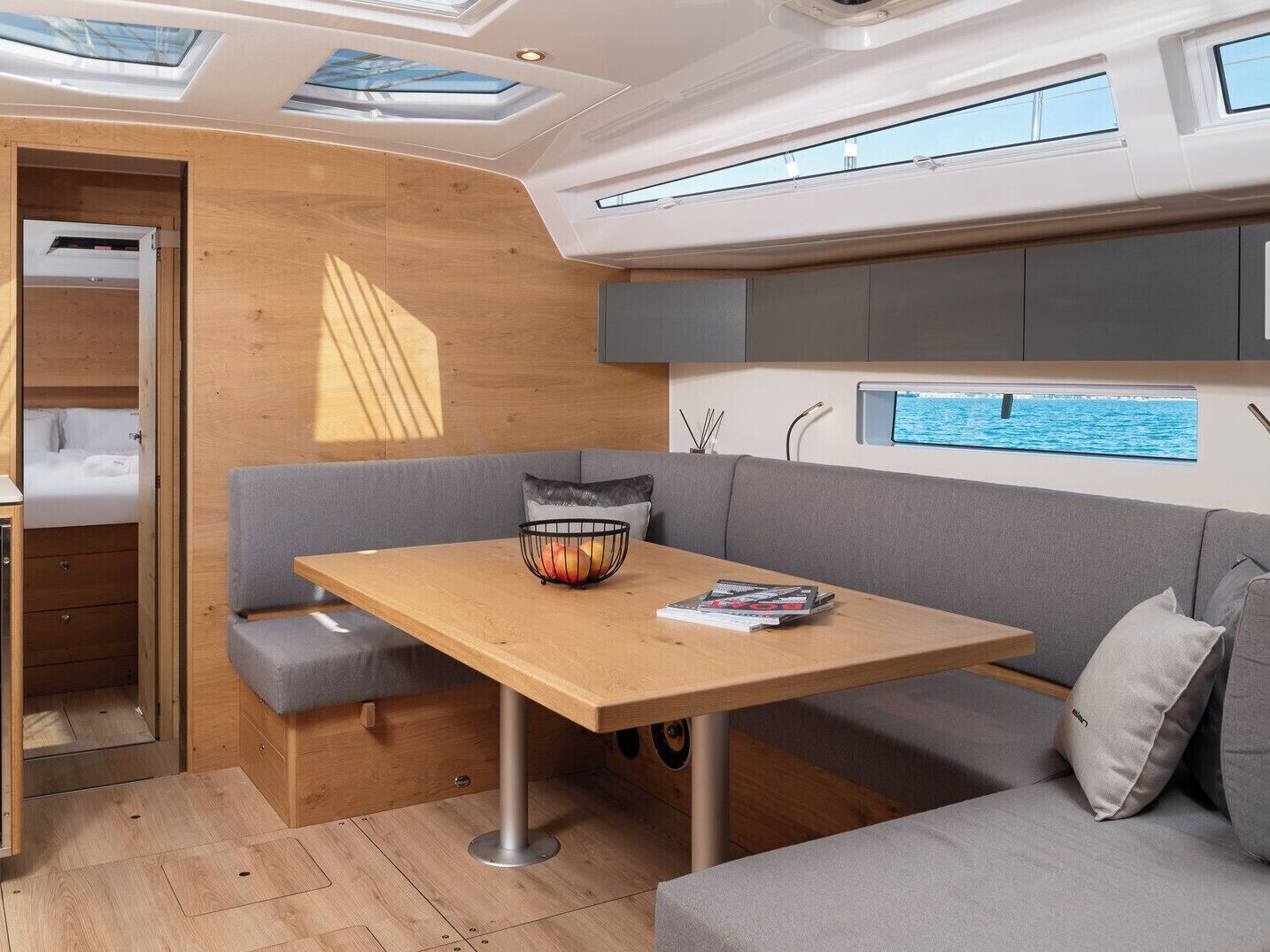 A compact, modern interior with a wooden table, grey seating, and a small window with a view of the sea.