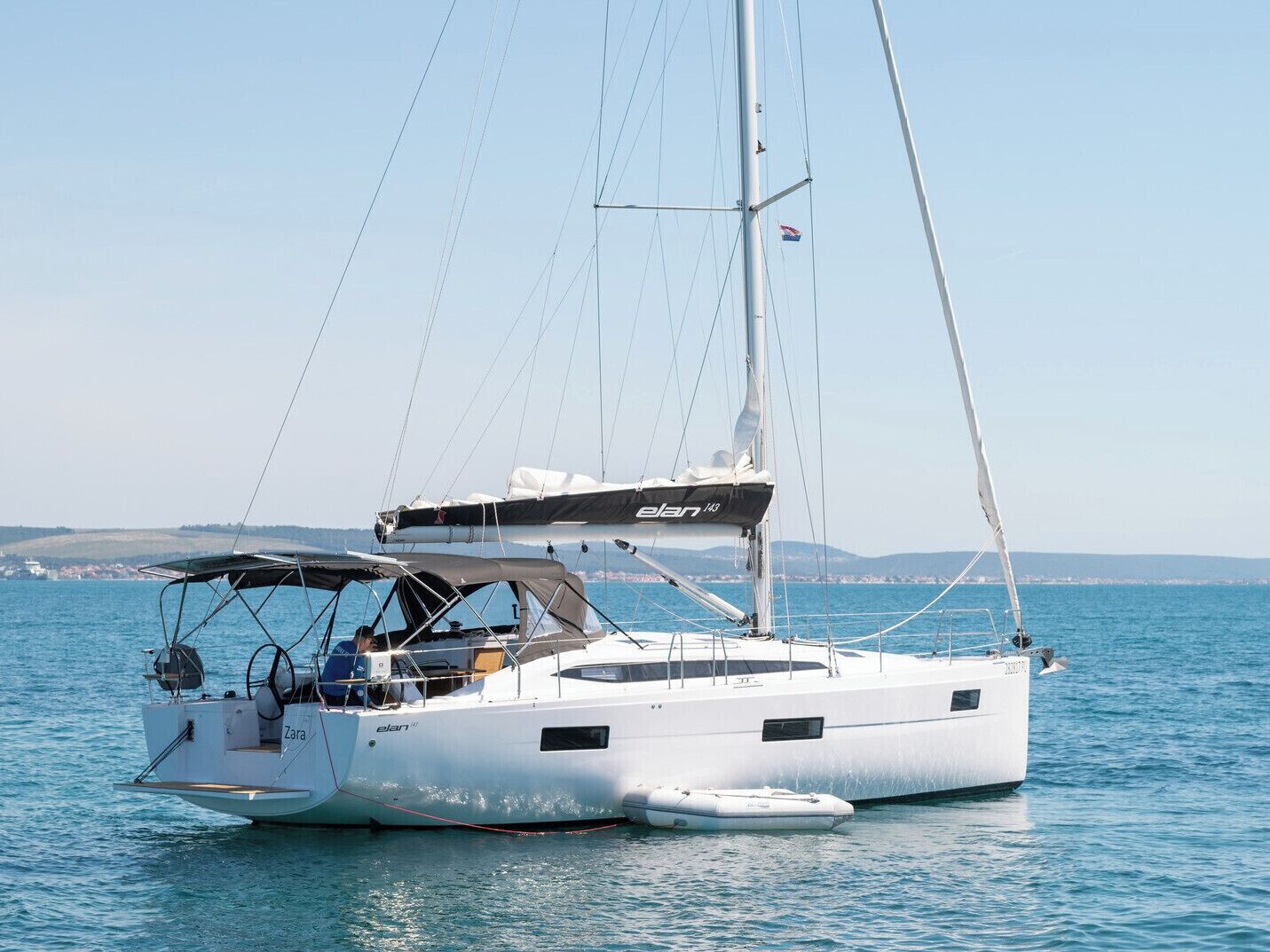 A sailboat named 'Zara' with a cabin and deck seating, docked in calm waters.