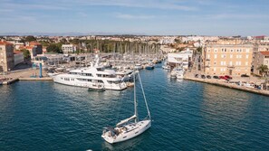 Ein Yachthafen mit mehreren angemeldeten Yachten, ein Segelboot im Vordergrund und Gebäude entlang des Ufers.