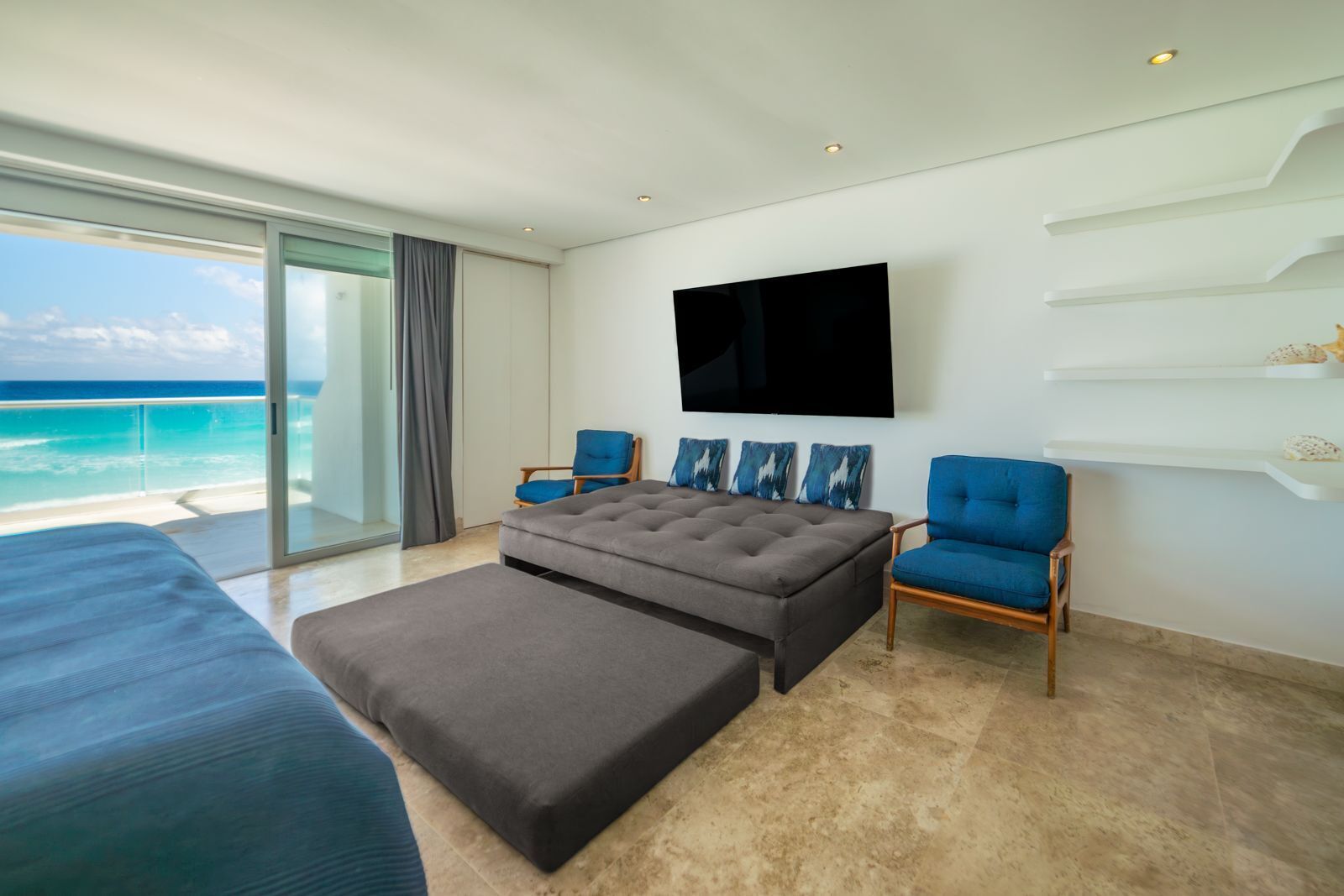 A modern hotel room with a large bed, a sofa, a TV, and a balcony with a view of the ocean.