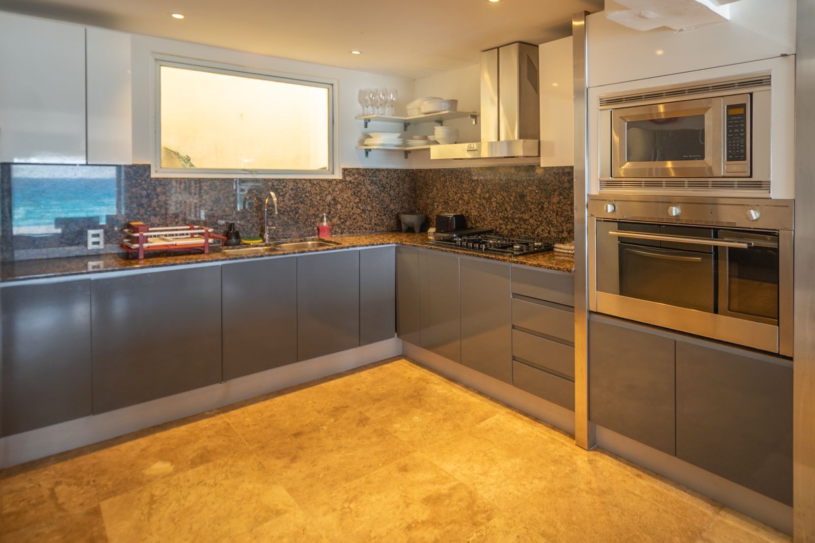 A modern kitchen with grey cabinets, a built-in oven, a microwave, and a granite countertop.