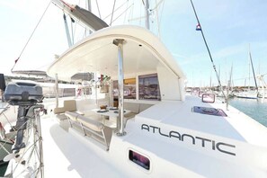 Eine Yacht namens ATLANTIC liegt in einer Marina mit einer überdachten Sitzgelegenheit und einem kleinen Tisch vor Anker.