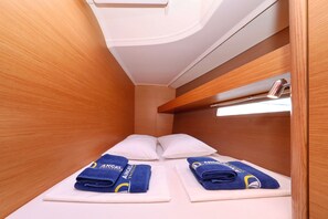 A narrow cabin with wooden walls, two beds with white pillows, and blue towels with a logo.