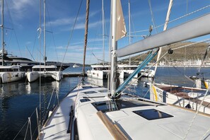 A marina with multiple sailboats docked, calm water, and a clear sky.