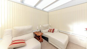 Een kamer met dakraam, twee witte banken, een klein houten bijzettafeltje en een witte bakstenen muur.