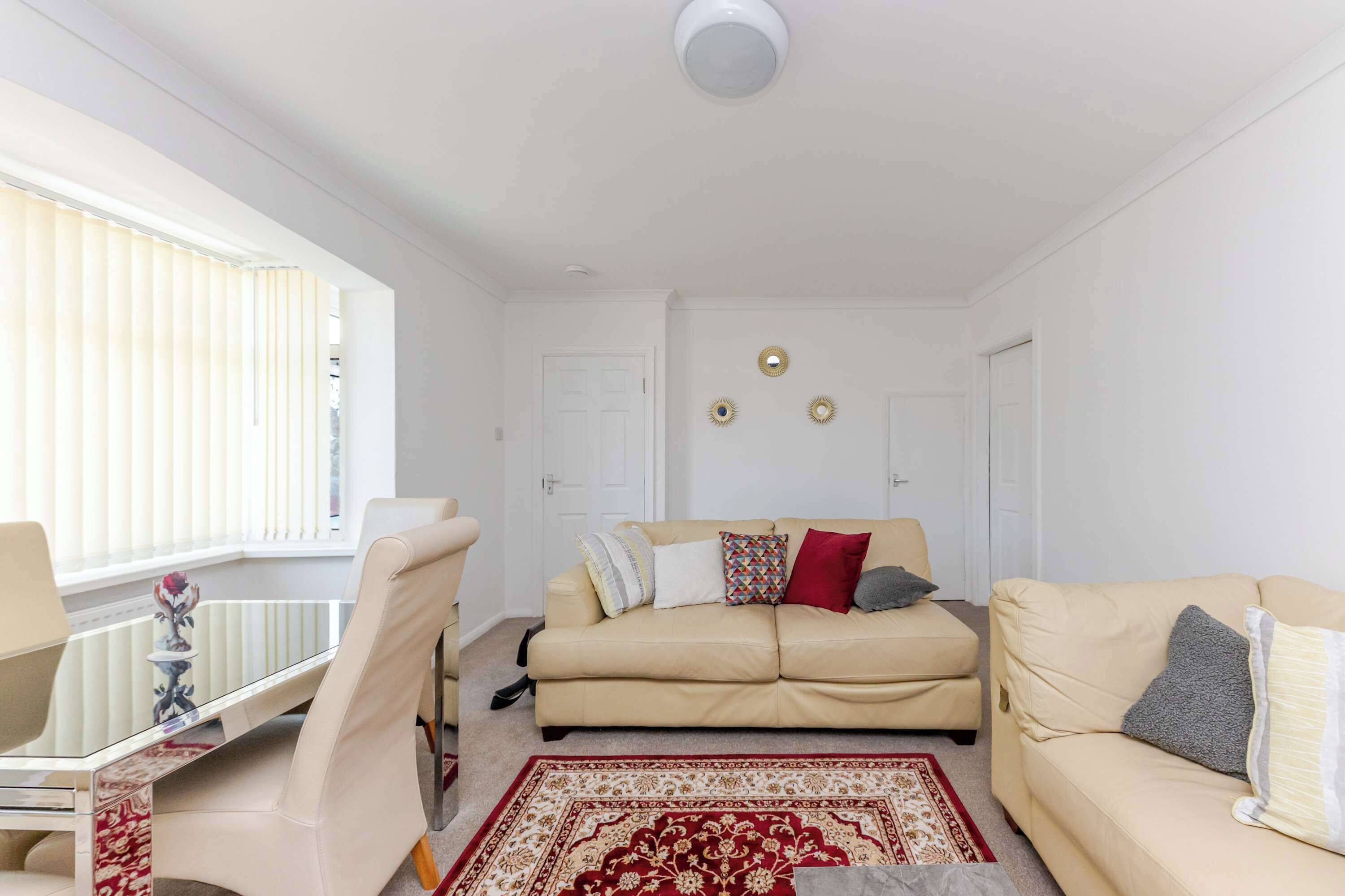 Un salon avec un canapé beige, une table basse en verre, un tapis aux motifs rouges et dorés, et un plafond blanc.
