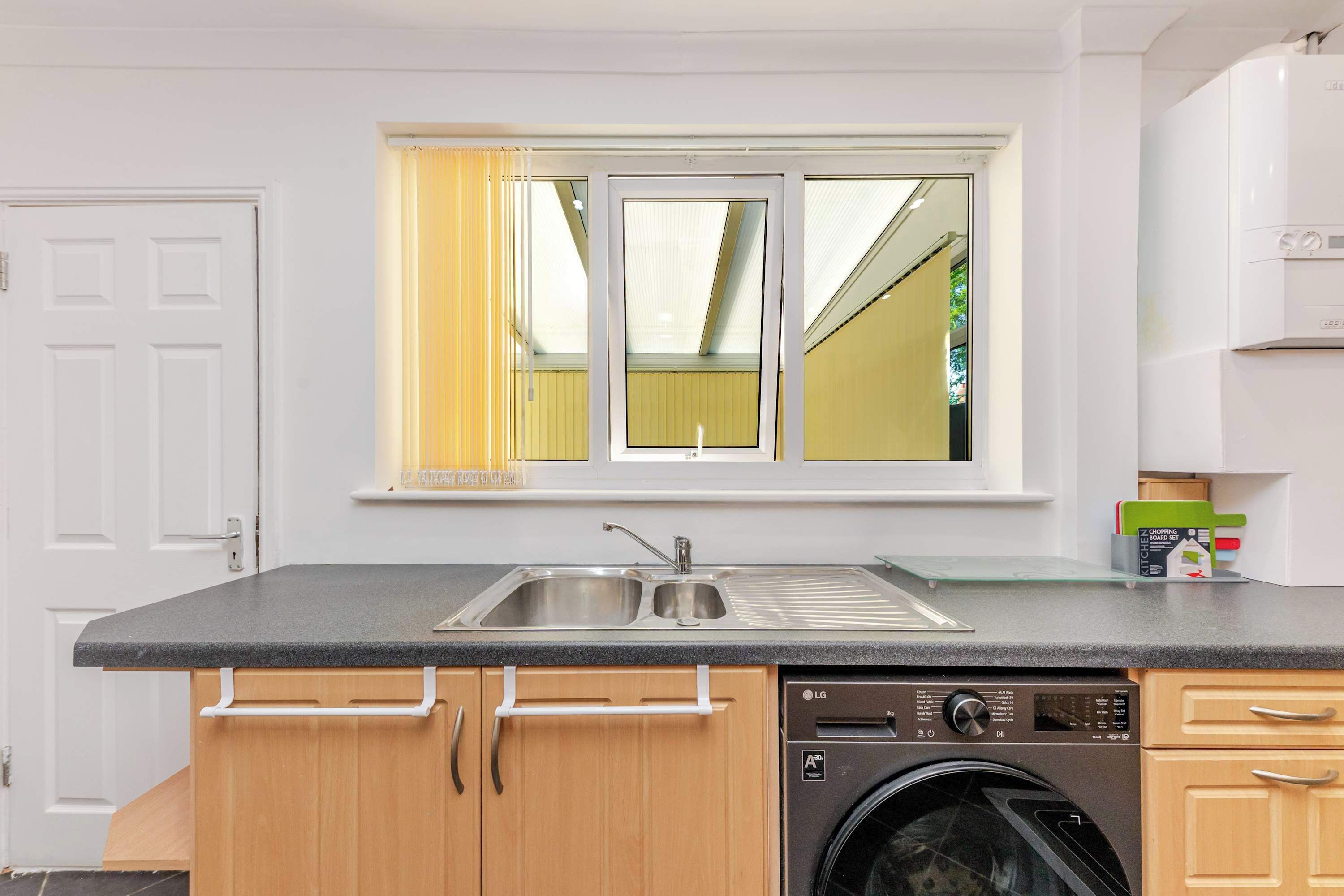 Eine kompakte Küche mit Waschmaschine, doppelter Spüle und einem Fenster mit Vorhängen.