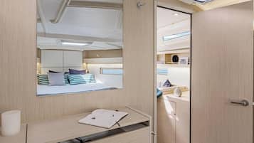 A compact, well-lit cabin with a bed, bedside table, and a mirror reflecting the room.