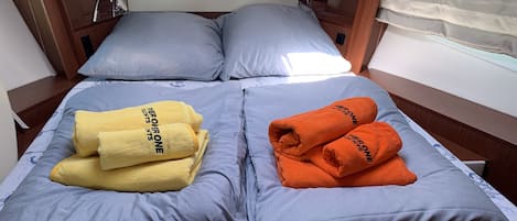 A bed with two pillows, a window with blinds, and two towels on the bed.