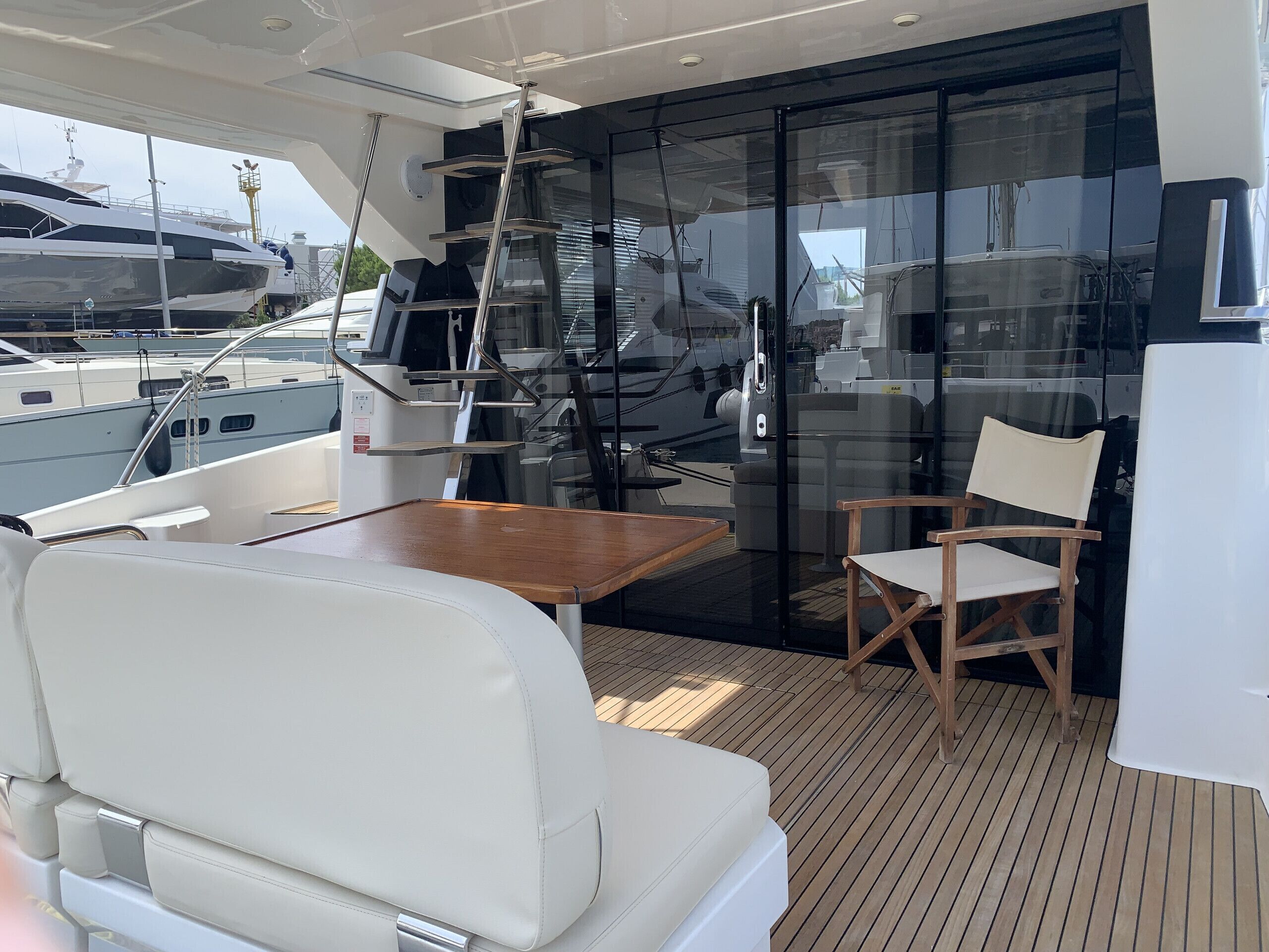 A yacht's deck with a table, chairs, and a glass door leading to the interior.