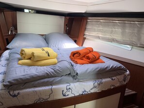 Ein Bett mit einem nautisch gestalteten Überwurf, zwei aufgerollte Handtücher und ein Fenster mit Vorhängen.