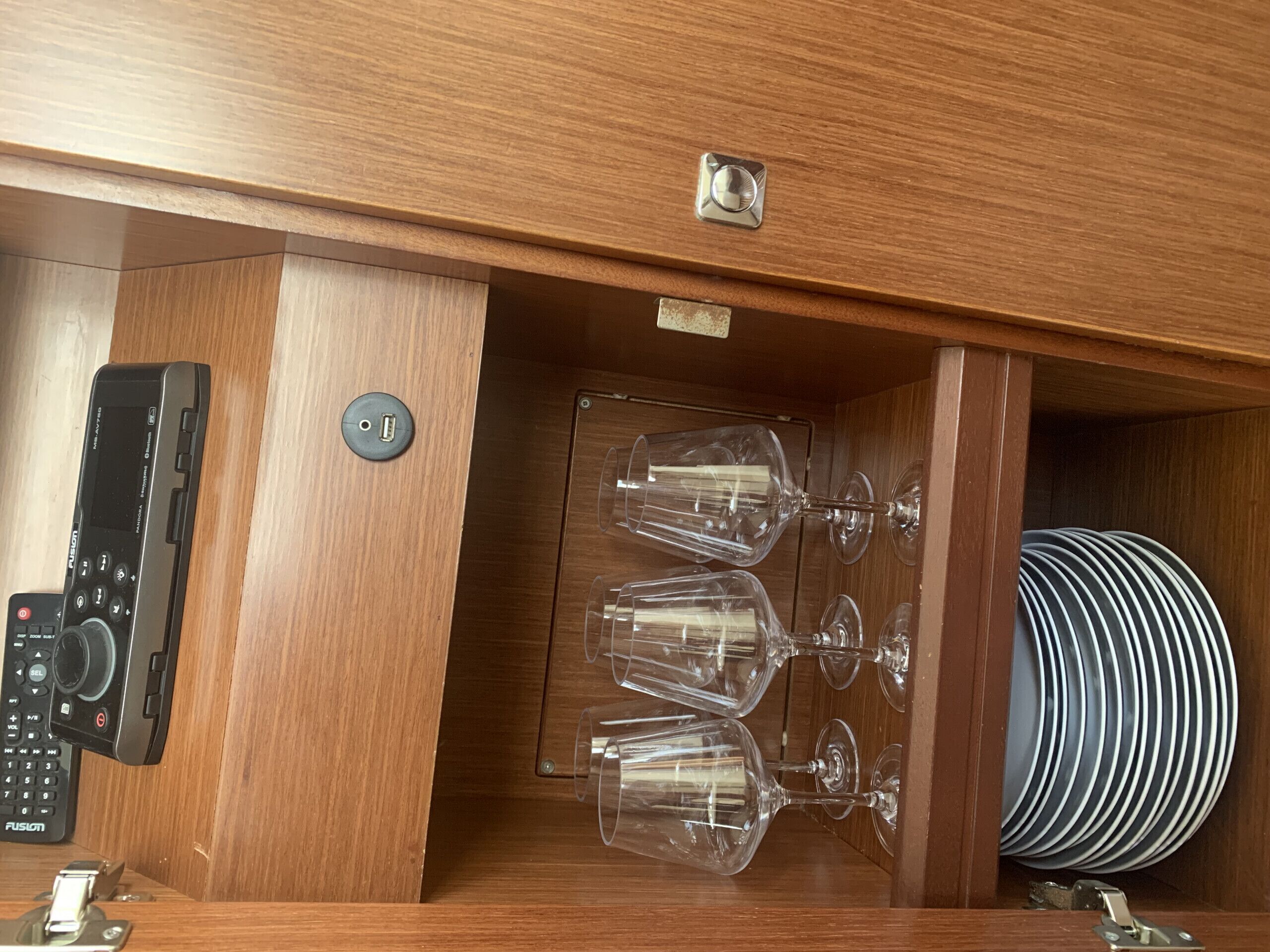Een houten kast met een bedieningspaneel, wijnglazen en gestapelde borden.