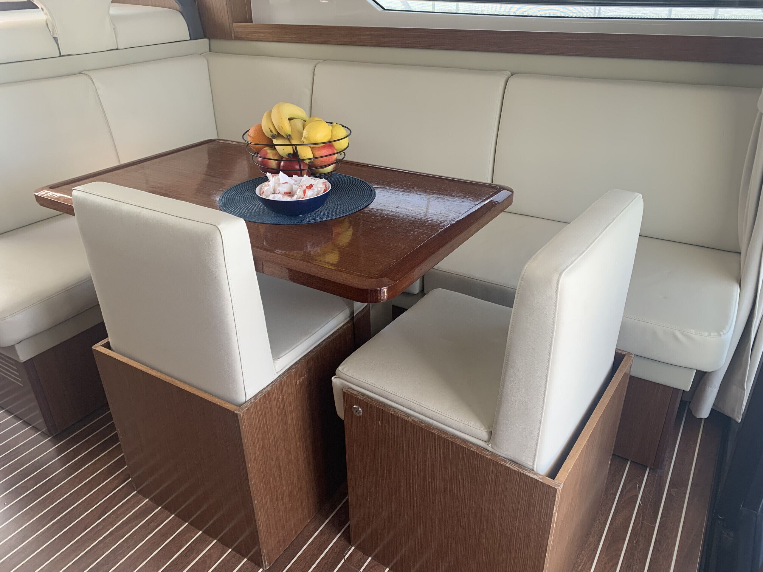 Interior de barco con zona de comedor que incluye una mesa, asientos acolchados y un frutero.
