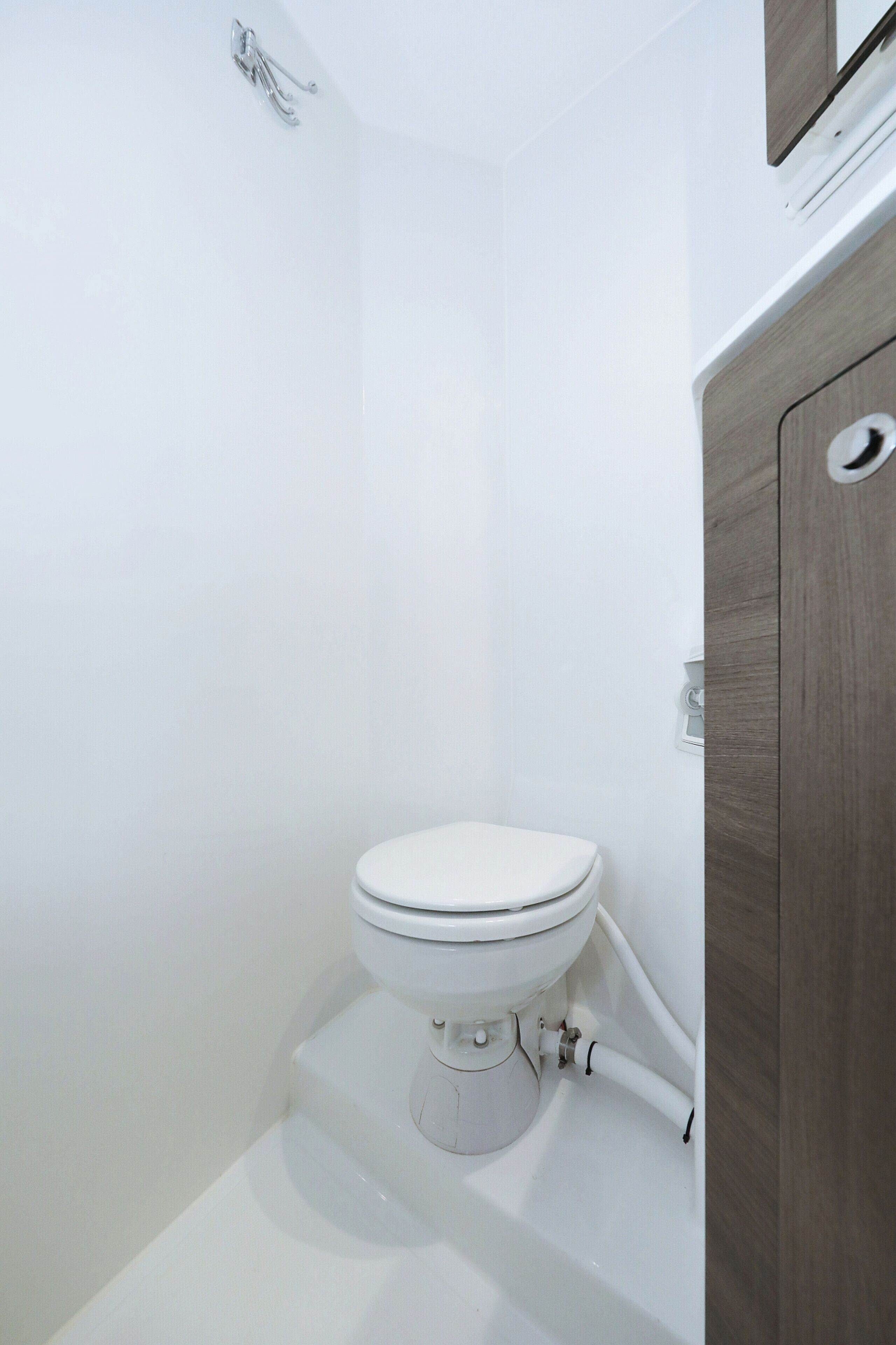 Eine weiße Toilette mit einem Holzschrank zur rechten Seite.