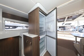 A compact kitchen with a built-in refrigerator, wooden cabinetry, and a window overlooking a marina. - Sibenik Sun and Beach Sailing Extravaganza: A Croatian Coastal Adventure (Vodice)