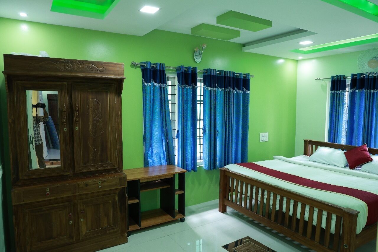A bedroom with a bed, a wooden wardrobe, a desk, and a window with curtains.