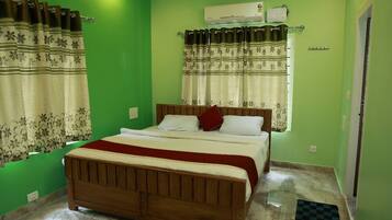 Een slaapkamer met een houten bed, groene wanden, behang met patroon, een airconditioningapparaat en een geruit vloerkleed.