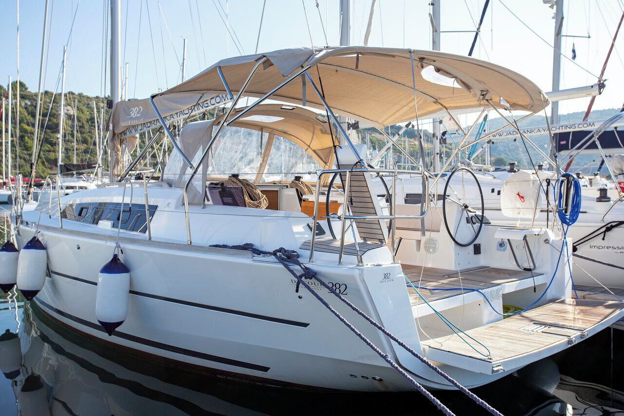 A sailboat docked at a marina with a covered deck, a seating area, and a steering wheel.