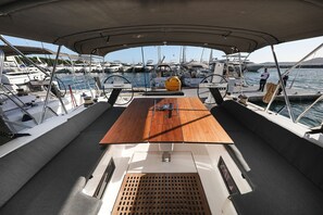 Ein Bootsdeck mit Holztisch, gepolsterten Sitzgelegenheiten und Blick auf andere Boote im Yachthafen.