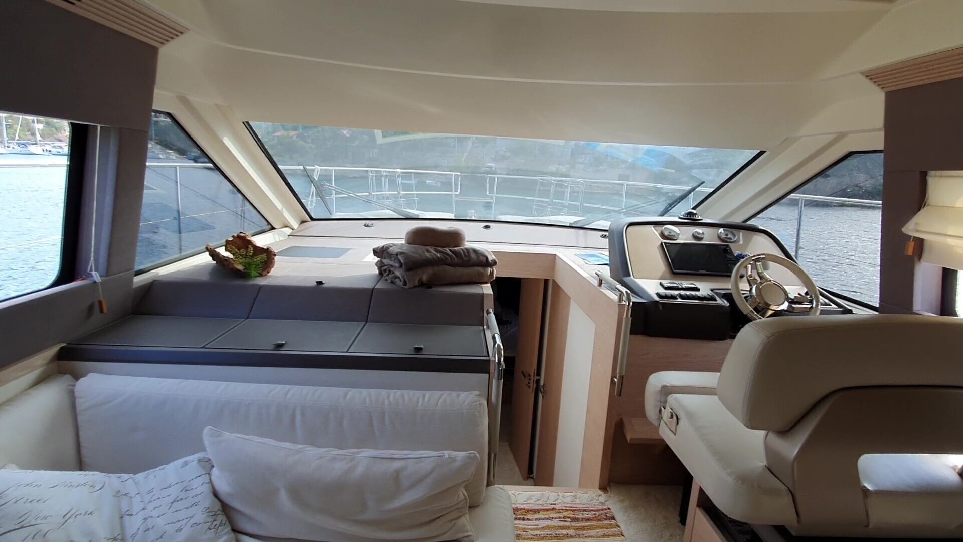 Interior de barco con cama, una mesita, timón y vista al agua.