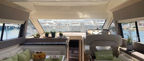 A boat interior with a dining area, seating, and a view of the marina.