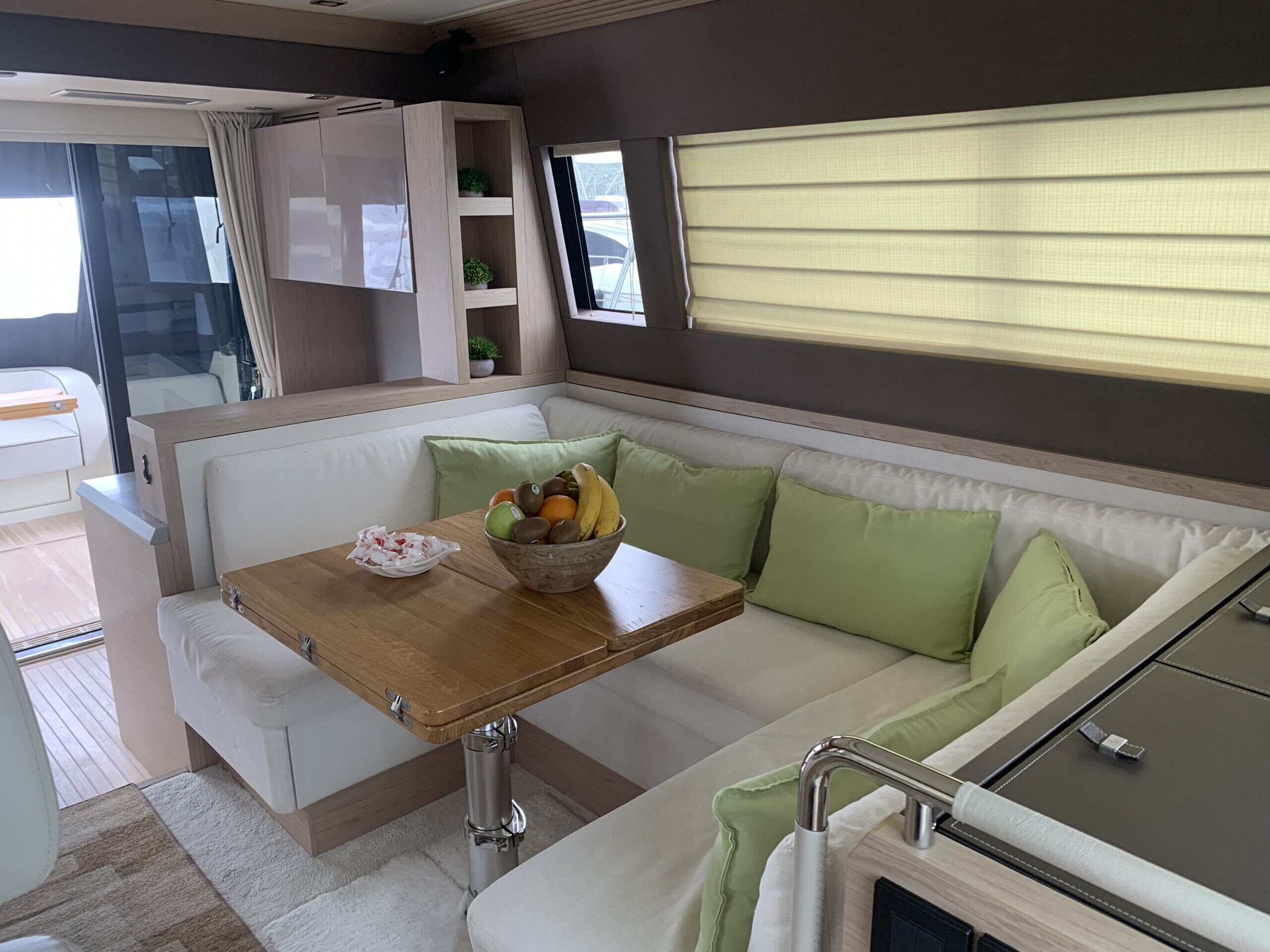 A compact living space with a sofa, a small table with a bowl of fruit, a window with blinds, and a kitchenette area.