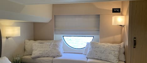A cozy cabin with a cushioned bench, a small table, a lamp, and a window with a view.