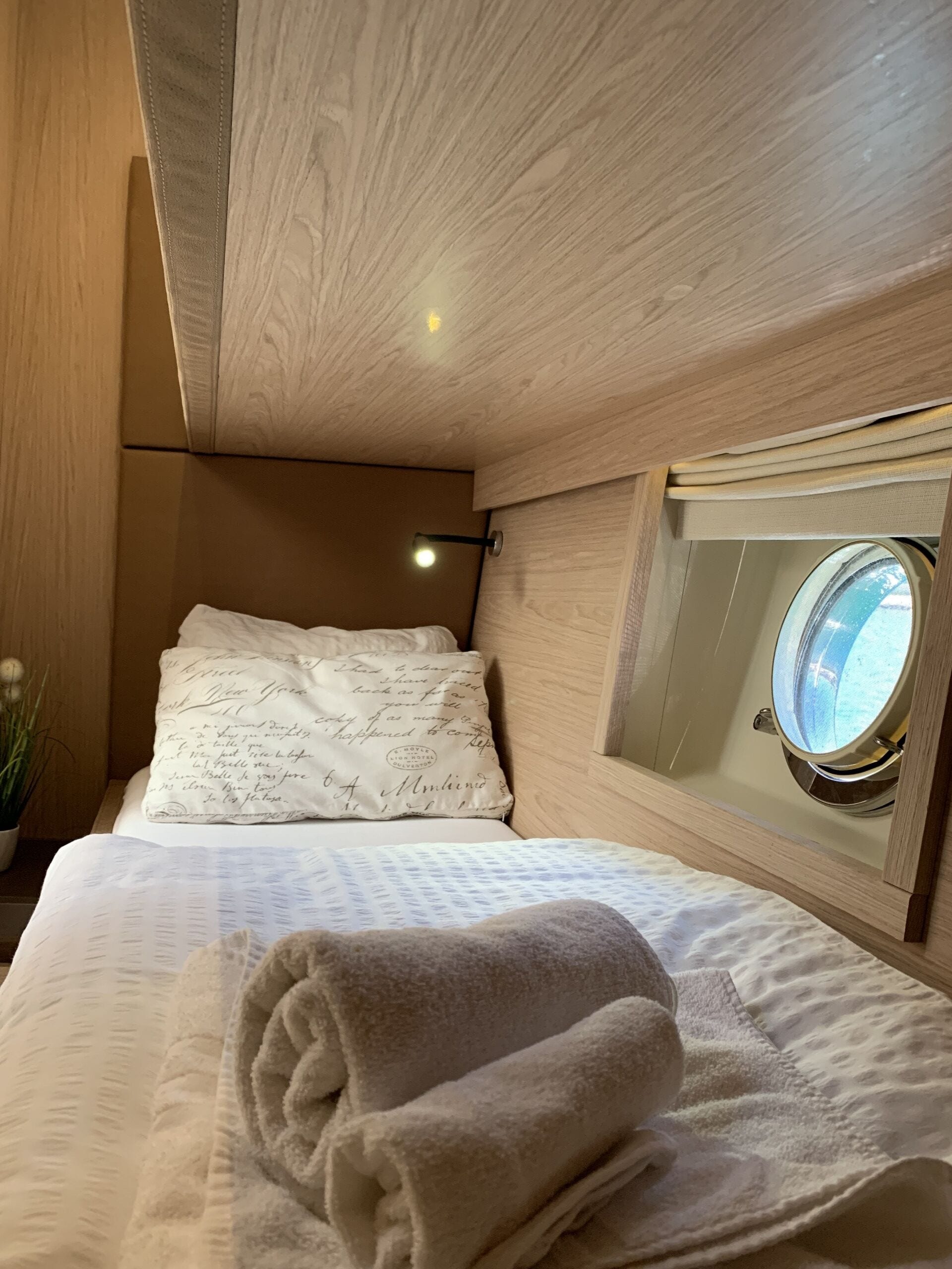 A cozy bedroom with a wooden ceiling, a bed with a rolled towel, a pillow with writing, and a window with a view.