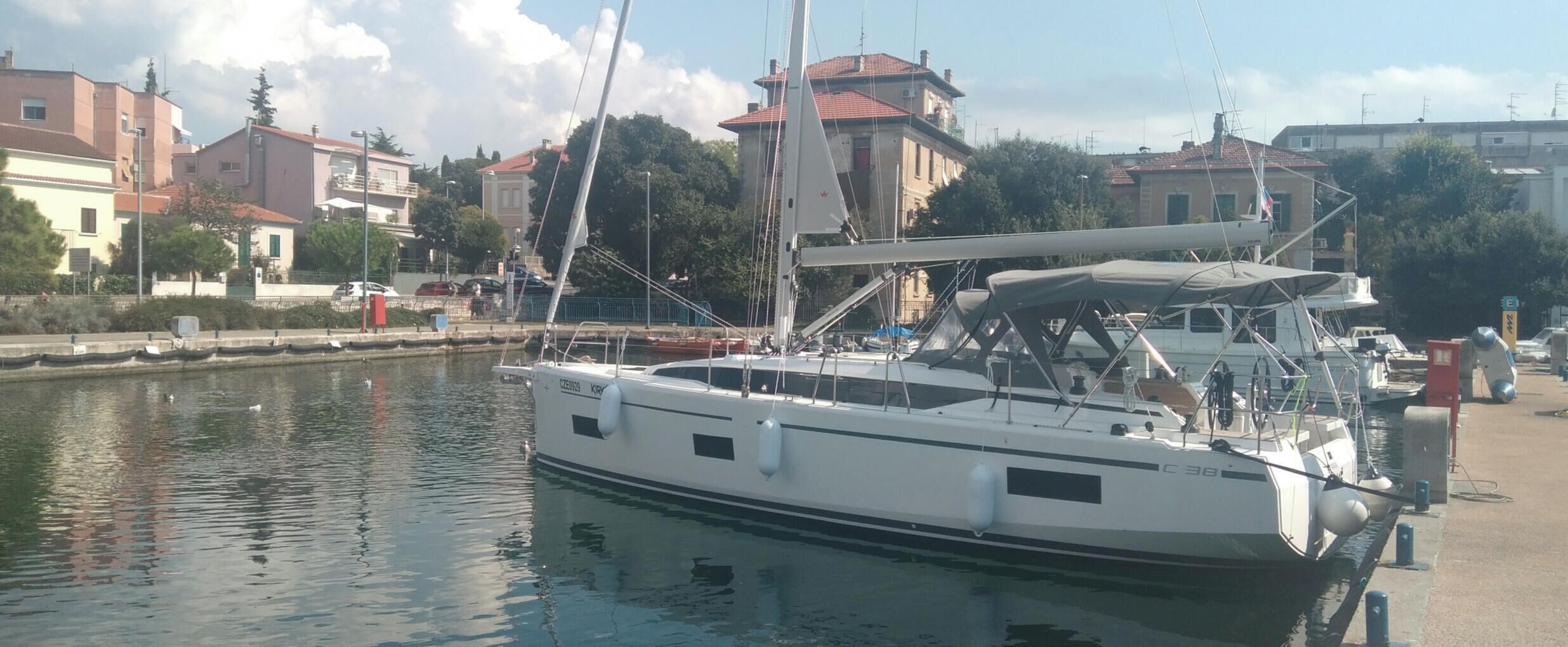 A marina with boats docked, a calm water body, and buildings in the background.