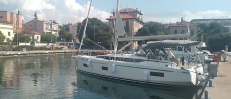 A marina with boats docked, a calm water body, and buildings in the background.
