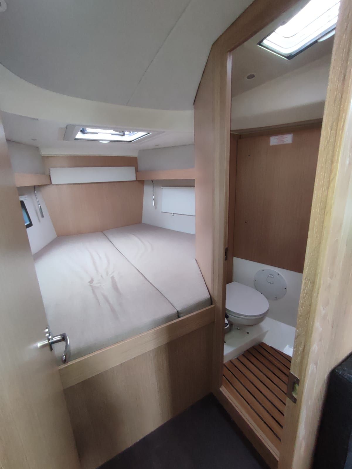 A compact, single-room boat cabin with a bunk bed, a toilet, and a skylight.