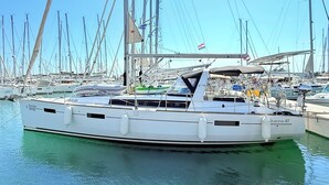 Un yate blanco amarrado en un puerto deportivo con varios otros barcos, cielo despejado y banderas.