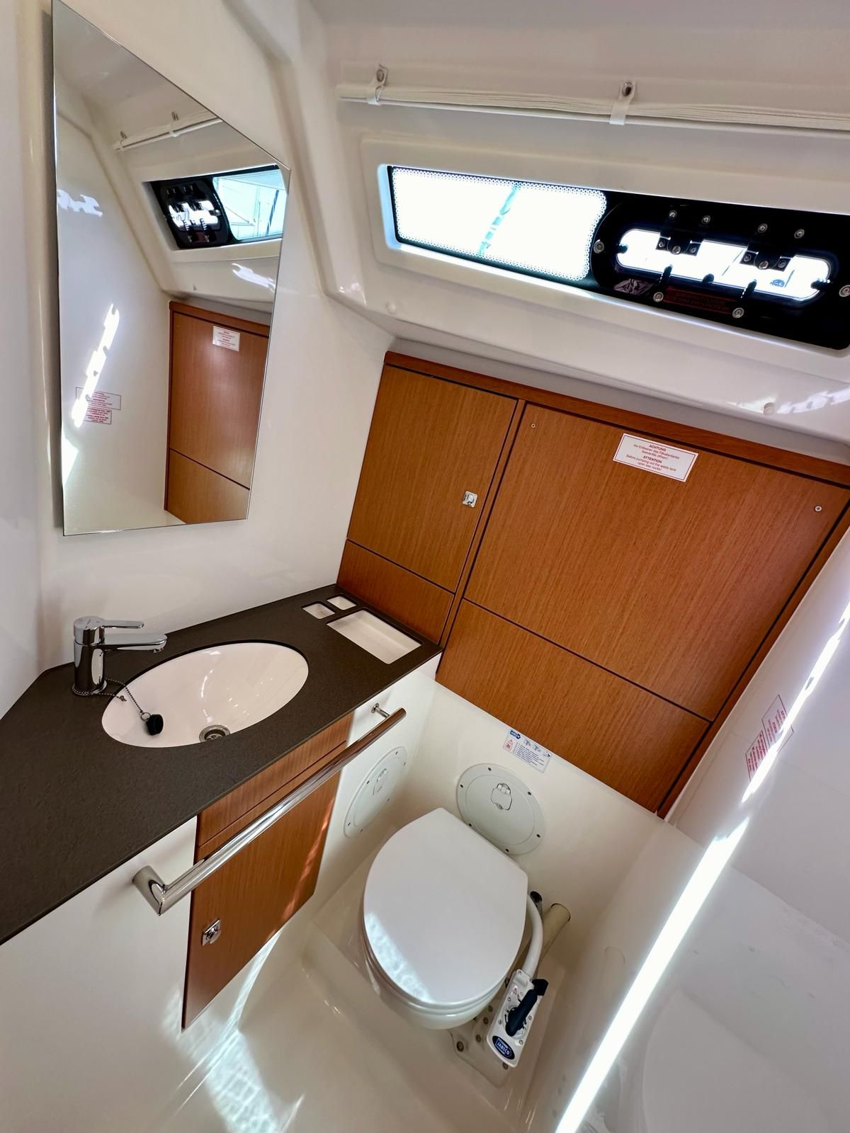 A compact bathroom with a white sink, a mirror, a toilet, and wooden cabinets.