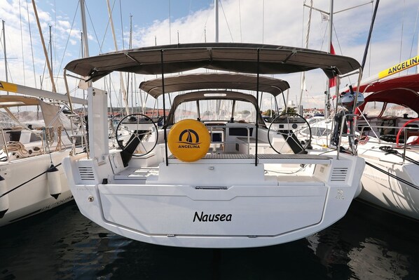 A white boat named 'Nausea' docked at a marina with other boats, a yellow 'ANGELINA' sign, and a clear sky. - Sibenik Sun and Beach Sailing Extravaganza: A Croatian Coastal Adventure (Vodice)
