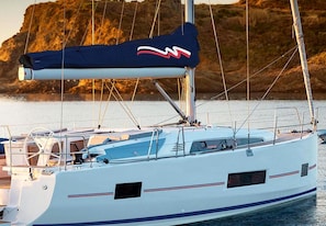 Ein Segelboot mit Kabine und Mast vor einer felsigen Küstenlinie.