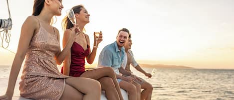 A group of people on a boat with a view of the sea and a sunset in the background.