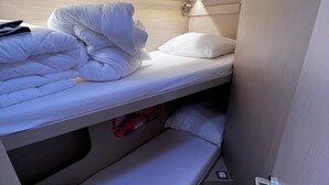 Ein Etagenbett mit weißer Bettwäsche, ein kleines Regal mit einem roten Gegenstand und eine Tür mit Griff.