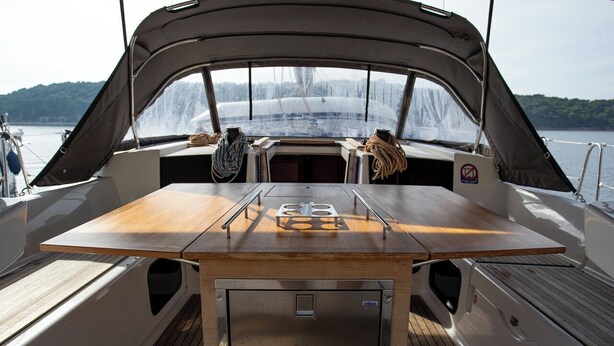 Het dek van een boot met een centrale tafel, een overdekt gedeelte en uitzicht op het water.