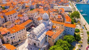 An aerial view of a historic city with a prominent church featuring a dome and bell tower, surrounded by tightly packed buildings with red-tiled roofs. - Sibenik Sunshine Sailing: A Luxurious Croatian Beach Experience (Sibenik)