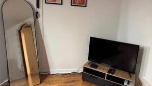 Une pièce avec un plancher en bois, un téléviseur à écran plat posé sur un meuble en bois, un grand miroir et deux tableaux encadrés accrochés au mur.