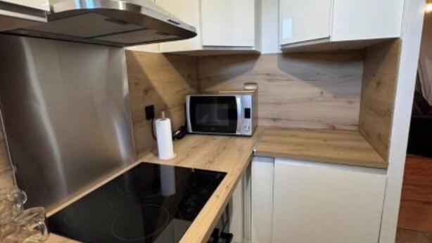 Une cuisine compacte avec des meubles blancs, une hotte de cuisinière en acier inoxydable, un four à micro-ondes et un plan de travail en bois.