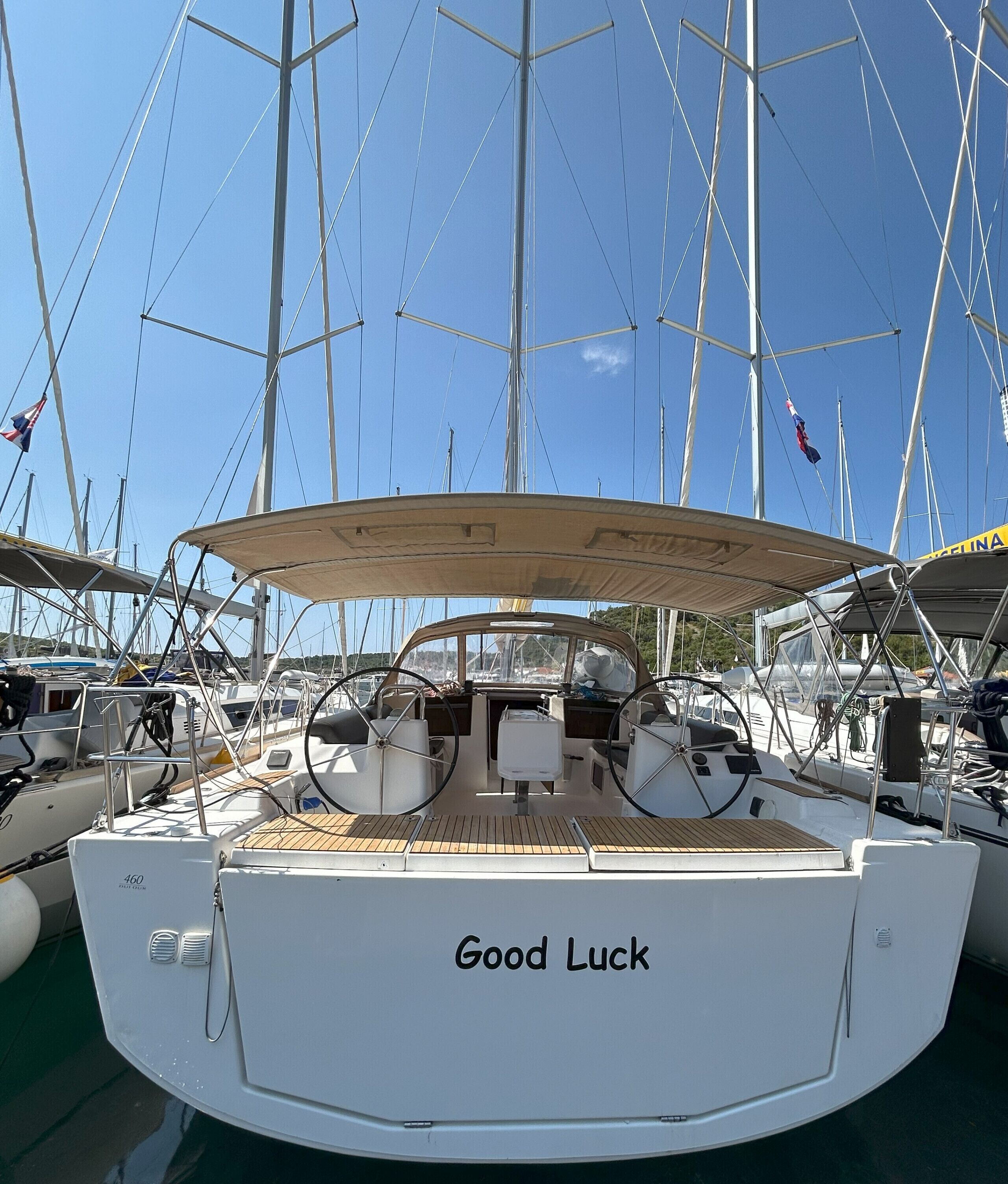 Um barco chamado 'Good Luck' atracado em um porto de iates, com outros barcos, céu claro e vista para a água.