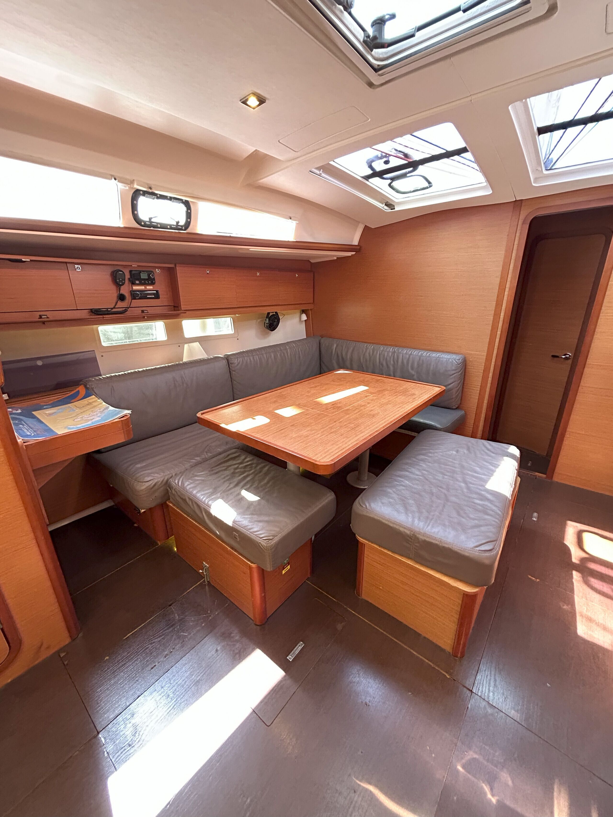 Interior de barco compacto com mesa de madeira, assentos acolchoados, painel de controle e claraboias.